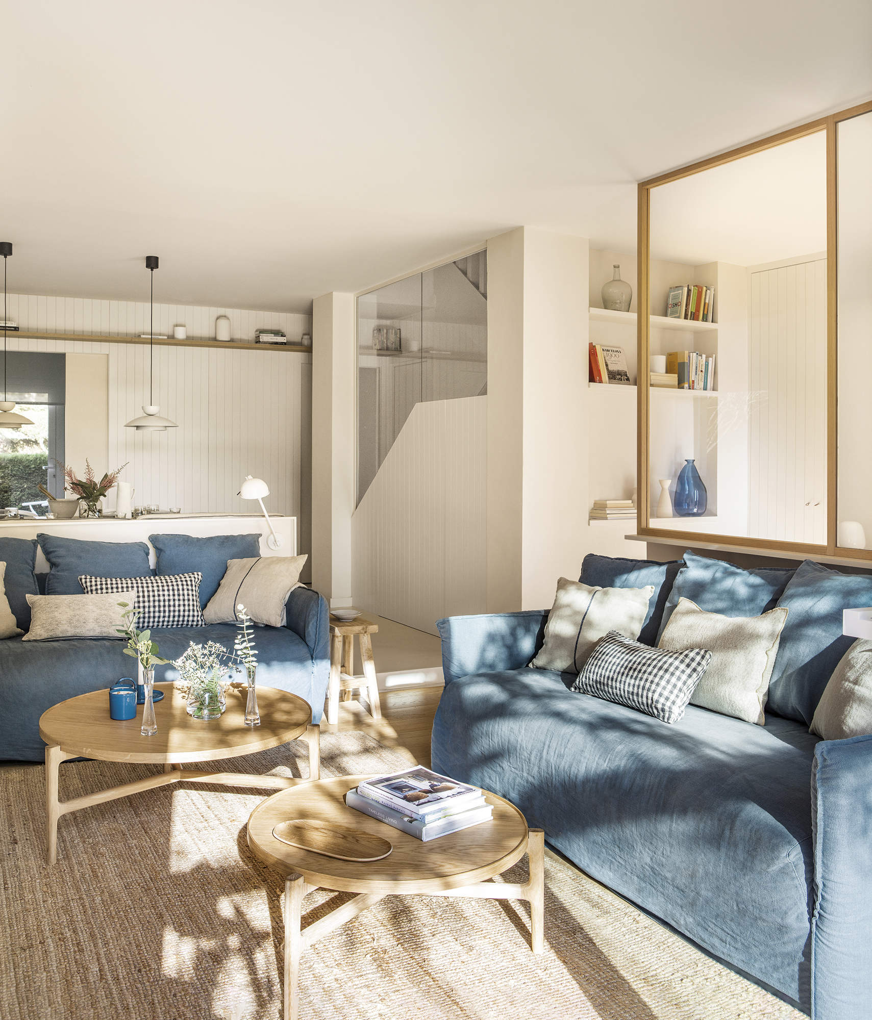 Salón con sofá azul abierto a la cocina, cerramiento de cristal y alfombra de fibra